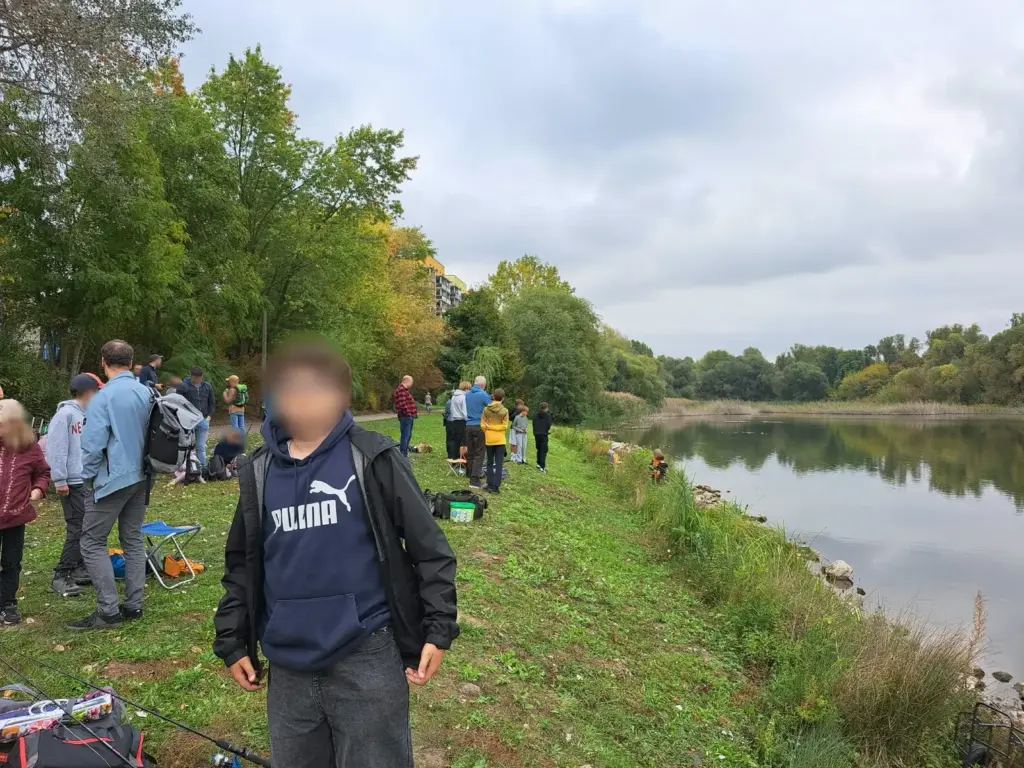 Jungangler steht am Ufer des Silbersees, im Hintergrund weitere Kinder und Betreuer beim Jugendangeln