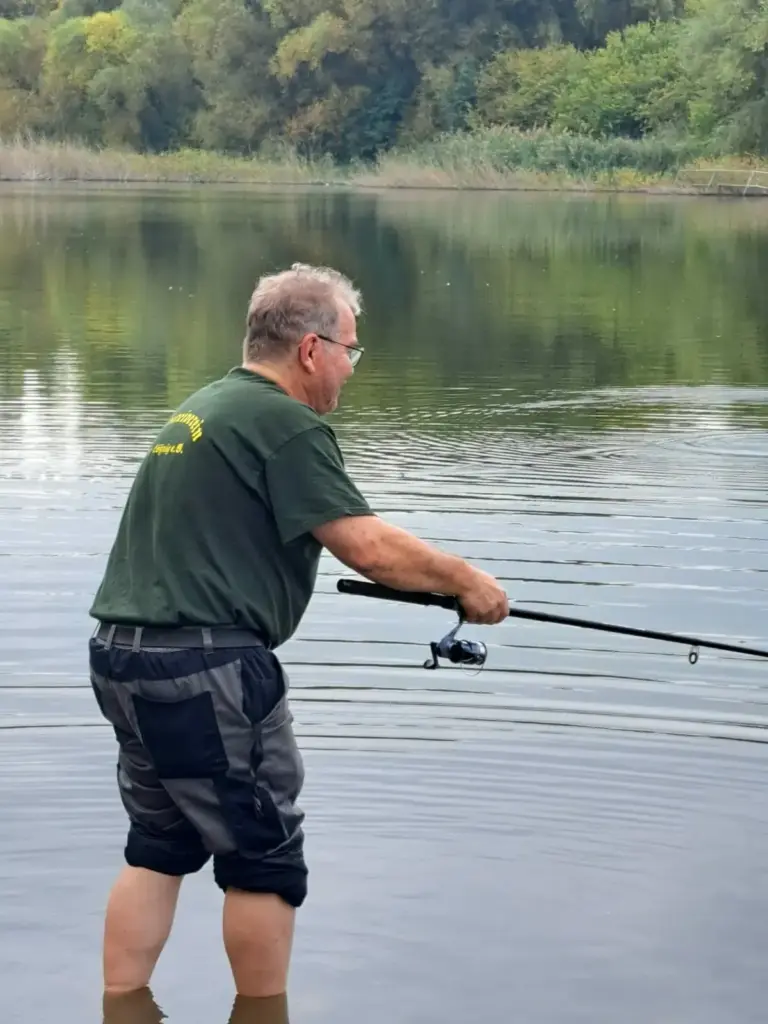 Betreuer im grünen Vereinsshirt steht im Wasser und angelt