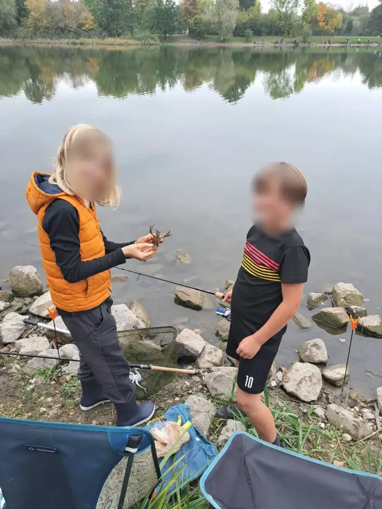 Zwei Kinder am Ufer, eines hält einen gefangenen Krebs in den Händen